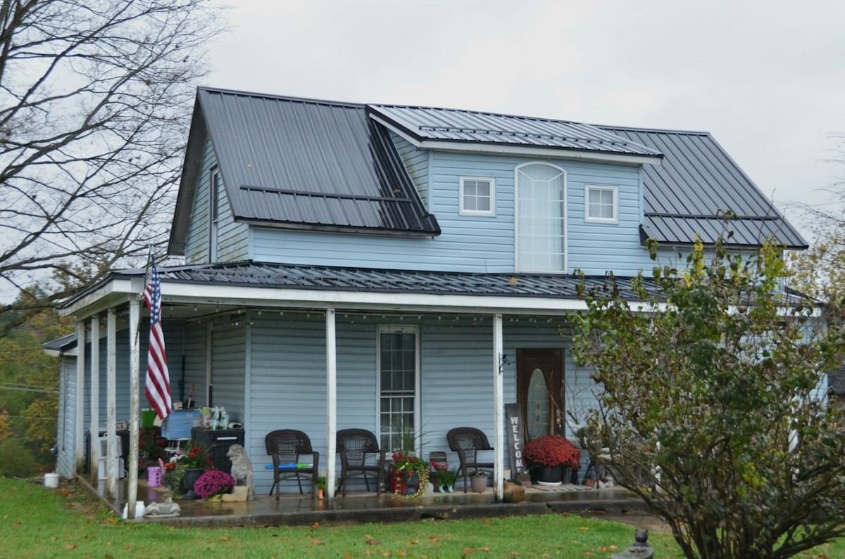 A blue farmhouse with a dark metal roof and a covered porch