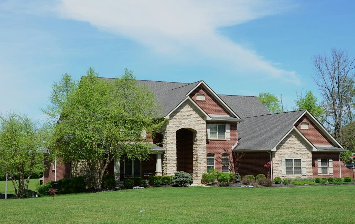 A two-story brick and stone house with a dark shingle roof and spring trees