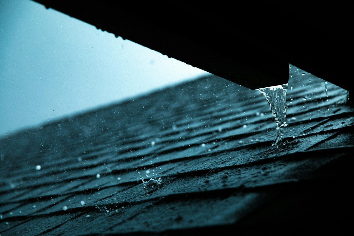Rainwater pouring off a roof edge onto wet asphalt shingles