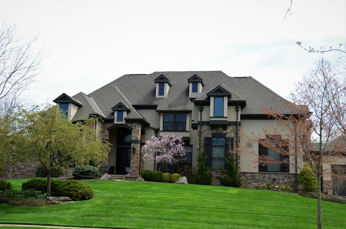 A stone and stucco house with several dormers on a steep shingle roof