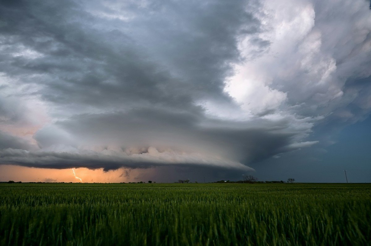 A large storm cloud with lightning over a green field