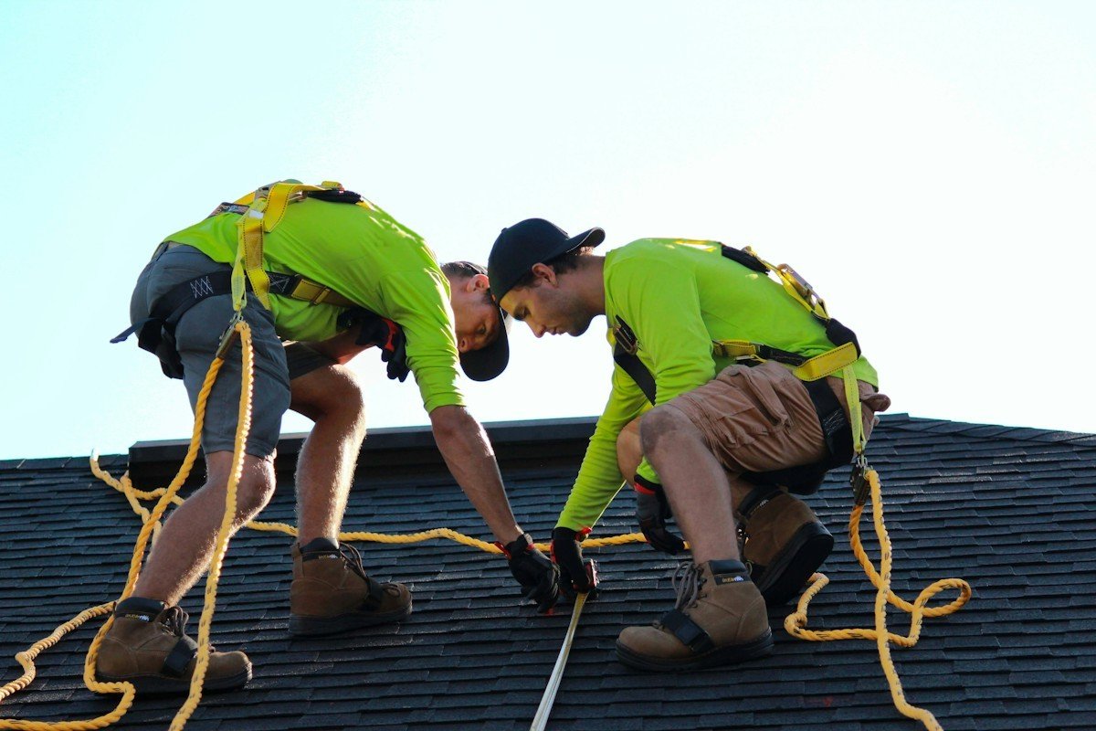 Two roofers in harnesses lining up a row of new shingles