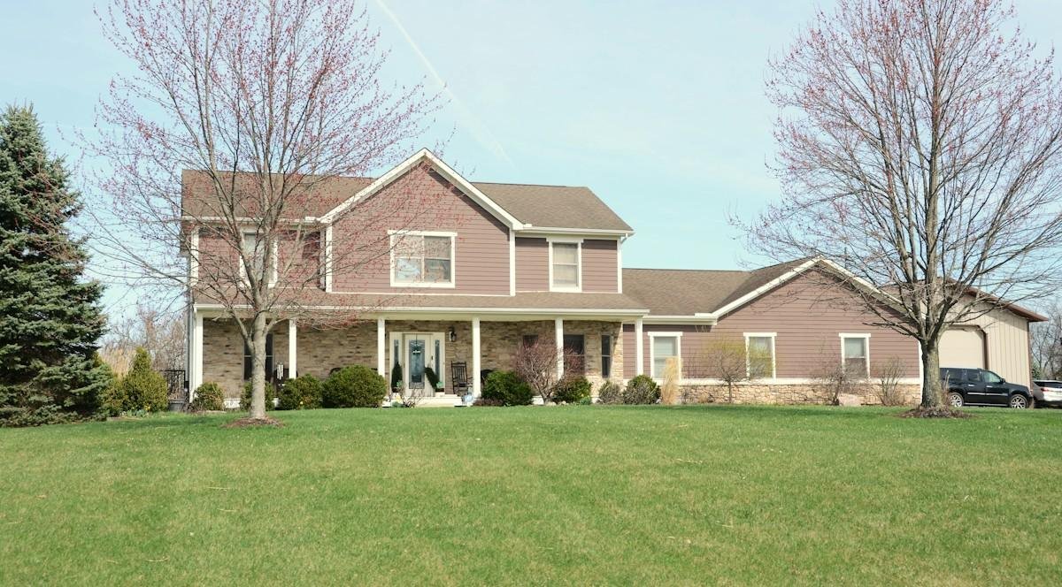 A two-story house with a covered porch and a brown shingle roof in early spring