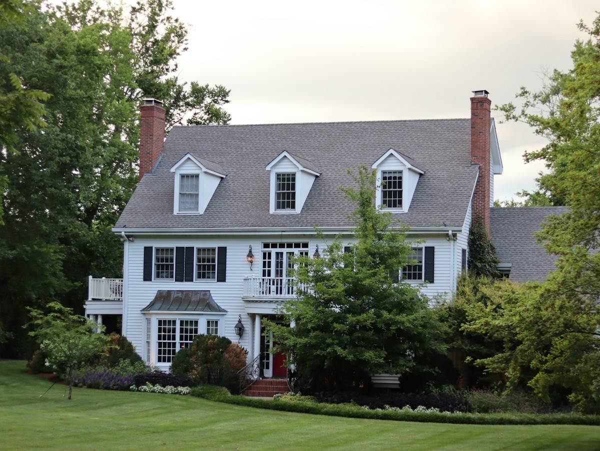 A white colonial house with three dormers and brick chimneys